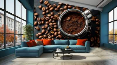 Close-up of a portafilter filled with ground coffee surrounded by roasted coffee beans on a dark surface, representing the preparation of espresso or coffee brewing. Wall mural