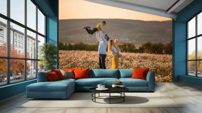 Father throws son in a field of daisies. Mother holds daughter in her arms. . Wall mural