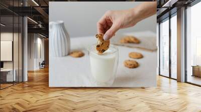 Female hand dipping cookies in milk. . Glass glass with milk and cookies. Wall mural