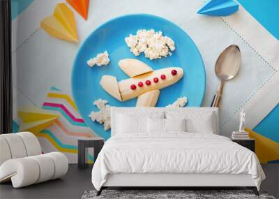 Fun food idea for kids. children's Breakfast: plane made of banana and clouds made of curd on a blue plate. dreams of flying. creative lunch of the future pilot Wall mural