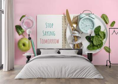 Quote Stop saying tomorrow Composition with cutlery, measuring tape, paper notebook, spinach, apple, water and alarm clock on color background. Diet concept Wall mural