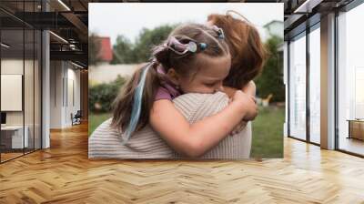 mother holds hugs and comforts upset little daughter outdoors Wall mural