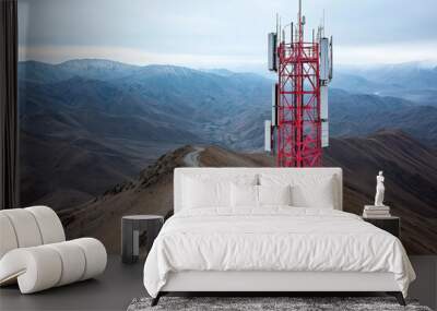 Red communication tower on a mountain ridge with antennas against a backdrop of expansive barren mountains. Cloudy sky over remote, rugged terrain. Wall mural