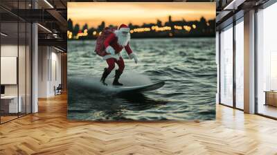 Santa Claus surfing with a sack of presents over ocean waves toward a vibrant city skyline at dusk Wall mural