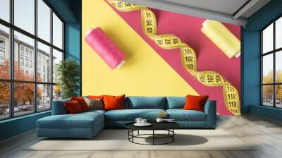 Bright yellow and pink background with contrasting spools of sewing thread. Wall mural