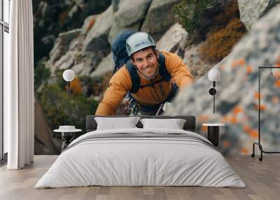 Mountain Climbing: Cheerful Caucasian Male Scaling a Mountain Side, wearing a helmet and a backpack.  Wall mural