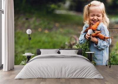 Adorable toddler smiling blonde girl holding carrots in domestic garden. Healthy organic vegetables for kids. Garden, vegetable, gardening. Picked Fresh Vegetables Just From The Garden Wall mural