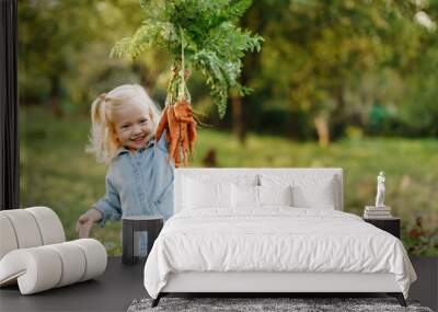 happy blond child girl picking fresh home growth carrot harvest from own garden. Seasonal autumn and summer work Wall mural