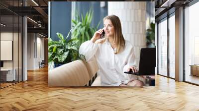 successful business woman sitting in cafe with laptop, working and talking on phone. office workplace with green plants. Wall mural