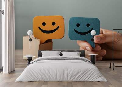 Two happy face speech bubble icons, one orange and one blue, with one being held by a hand, symbolizing communication and positivity. Wall mural