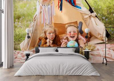 Two little sisters laughing and making faces laying next to wigwam decoration. Wall mural