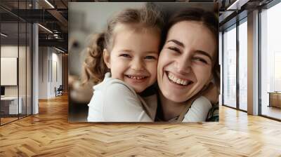 Woman and young girl hugging and smiling warmly at the camera in a cozy indoor setting. Wall mural