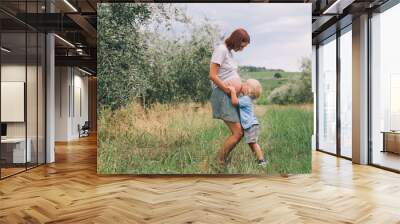 Child boy kissing belly of pregnant her mother on nature background. Wall mural