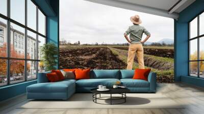 Female farmer standing proudly in agricultural field. Smiling thoughtful woman in plowed field background. Wall mural