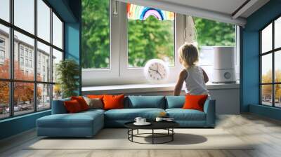 Little girl looks out window at home at spring time. Wall mural