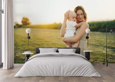 Loving mother and baby at sunset. Beautiful woman and small child in nature background. Concept of natural motherhood. Happy healthy family at summer outdoors. Positive human emotions and feelings. Wall mural