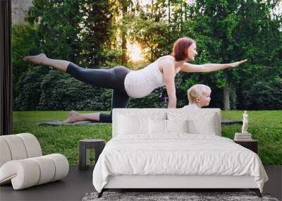 pregnant woman doing yoga with son on nature outdoors. Wall mural