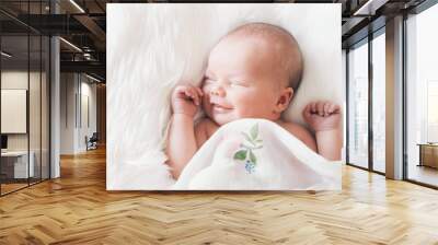 Sleeping smiling newborn baby in a wrap on white blanket. Wall mural