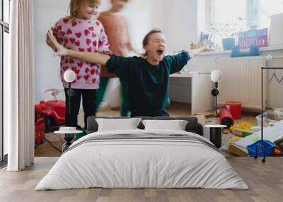 Stressed out mother sitting on floor while children running around her. Wall mural