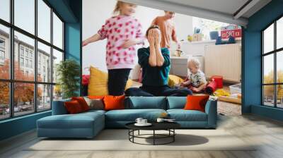 Stressed out mother sitting on floor while children running around her. Wall mural