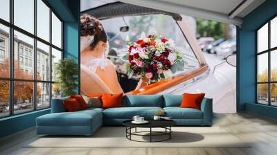 Beautiful young happy bride sitting in cabriolet. Bride with flowers boquete in the hand Wall mural