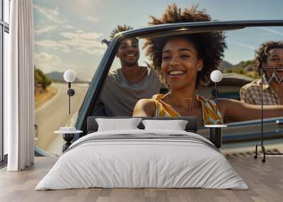 A African American woman with curly hair and a big smile sits in the front seat of a convertible with two men behind her. They are all laughing and seem to be enjoying a road trip Wall mural