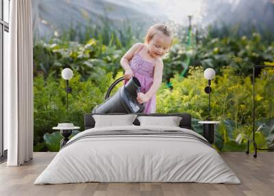 A cute toddler girl with a big watering can waters cabbage in the vegetable garden in summer, helping children in the garden and taking care of plants Wall mural