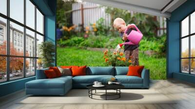 Child boy watering flowers in garden from can Wall mural