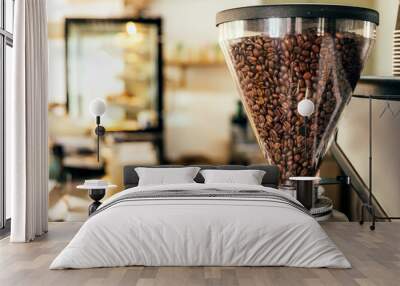 Coffee beans in a big glass grinder machine holder with blurred background of a cafe. Wall mural