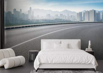 Curved asphalt road leading to a modern city skyline. Urban landscape background with copy space Wall mural