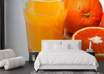 A glass of orange juice on the white background stands next to two whole oranges and sliced red orange Wall mural