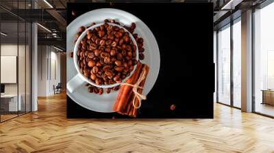 A white cup full of coffee beans stands on a white saucer, which stands on a black background Wall mural