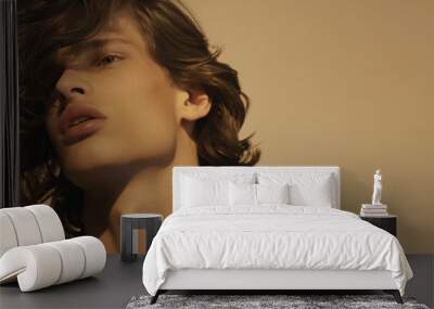 Close-up portrait of a young man with wavy hair, soft lighting, and a contemplative expression Wall mural