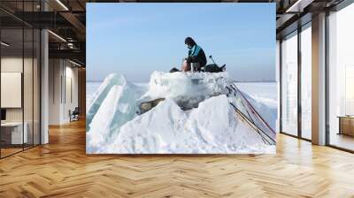 The man putting thermoses for a lunch on an ice block of the opened river Wall mural