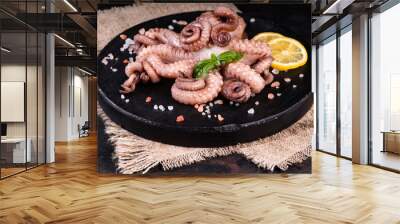 Raw octopus tentacles on a black round plate on a black background with slices of lemon and green leaves of basil and salt. Sea food. Wall mural