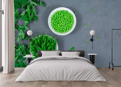 Two white bowls of fresh young green peas with stitches and peeled leaves on the background of shoots, sprigs of young green peas on a gray table. View from above. Close-up. Selective focus. Defocus. Wall mural