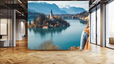 Young girl with backpack in hat stands on top of cliff on the shore of lake looking into the distance at old castle of Bled. Close-up. Generative Ai content Wall mural