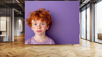 A boy with red hair and blue eyes is looking at the camera. He has a scruffy appearance and he is sad. a close up head shot of a red haired young boy pulling a funny face on a plain purple background Wall mural