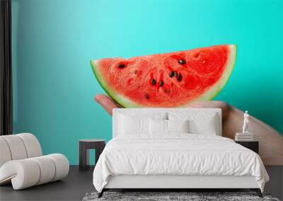 A hand holding a slice of watermelon. The watermelon is cut in half and is placed on a blue background. banner of Hand with piece of ripe watermelon on blue background Wall mural