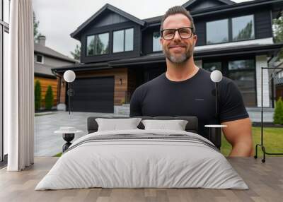 A man in a black shirt stands in front of a large house. He is smiling and he is happy Wall mural