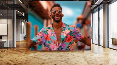 A man in a floral shirt is smiling and posing for a picture. a very happy young 30 year old dominican man with beach shirt and sunglasses walking while dancing up and down a very colorful street Wall mural