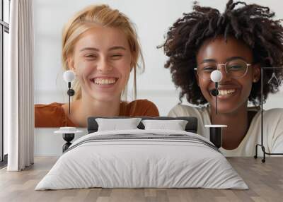 A two woman are smiling at the camera while looking at a laptop. The woman is wearing glasses. Scene is happy and friendly. photo with white background, two teachers smiling and using a laptop Wall mural