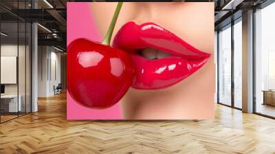 A woman is holding a cherry in her mouth. The cherry is red and shiny. The woman's lips are also red and shiny. The image has a playful and fun mood Wall mural