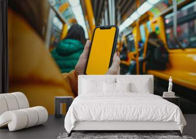 A woman is holding a phone in a subway car. Close-up photo of a girl's hand holding an iPhone inside a yellow subway car, with the focus on the phone's screen displaying a yellow screen Wall mural