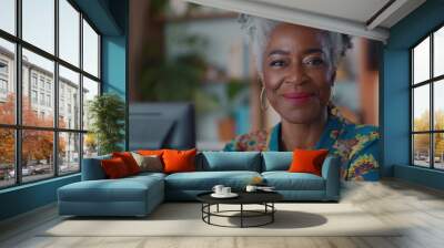 A woman with a big smile on her face is sitting in front of a computer. She is wearing a colorful shirt. a 60 year old attractive black woman typing on desktop computer with a smile at home Wall mural