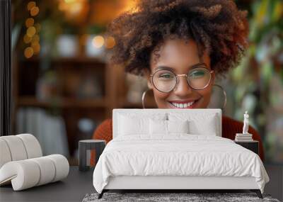 A woman with curly hair and glasses is smiling at the camera. She is wearing an orange sweater. female entrepreneur extremely happy because she starts making money in her online store Wall mural