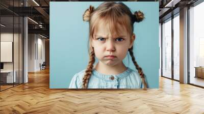 A young baby girl with a ponytail and a frowning face. She is wearing a shirt. Portrait of cute little upset girl, naughty kids idea Wall mural