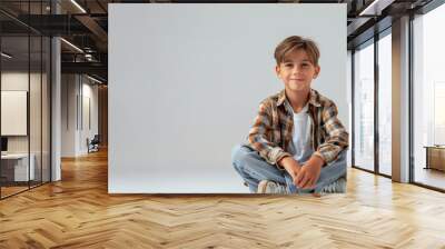 A young boy is sitting on the floor with his hands on his knees. He is smiling and looking at the camera. a white background, A 12-year-old handsome boy sits on the floor Wall mural