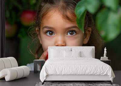 A young girl is holding a red apple in her hand. She is looking at the camera with a smile on her face Wall mural