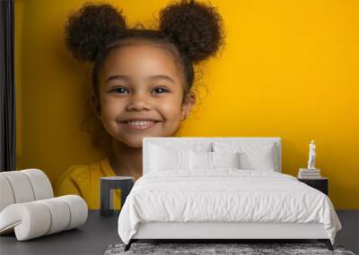 A young girl with curly hair is smiling at the camera in a yellow shirt. Concept of happiness and warmth, as the girl's smile and the bright yellow color of her shirt create a cheerful atmosphere Wall mural